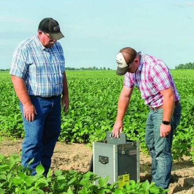 Tim Jackson, left, and son Evan check the water level control structure that helps control nutrient runoff from the field. Plates called stoplogs can be added or removed to adjust water level/flow.